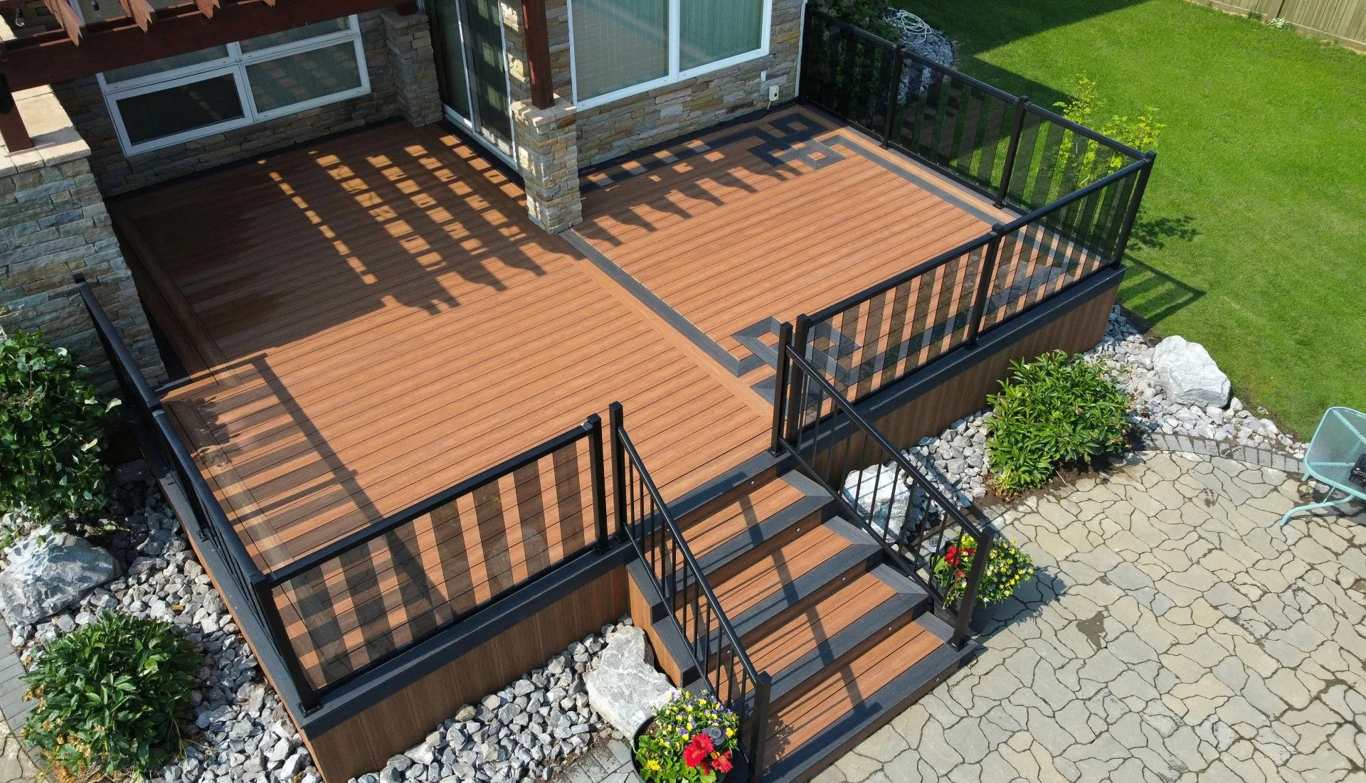 Two-tone composite deck with Celtic knot inlay and black glass railings next to a stone home